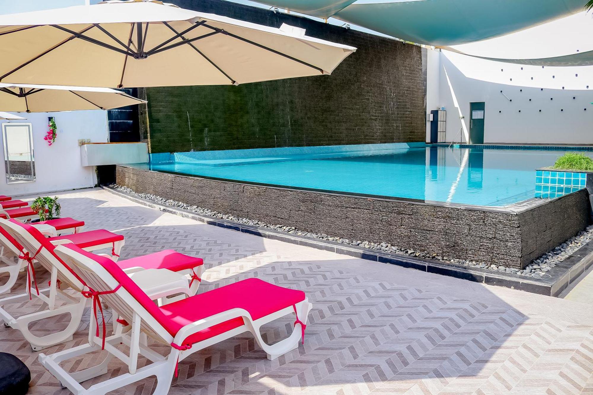 Lagoona Beach Luxury Resort And Spa Manama Exterior foto The photo shows a pool area featuring a rectangular swimming pool with clear blue water. Surrounding the pool are light-colored lounge chairs with pink cushions, positioned under large umbrellas for shade. The pool is bordered by a textured wall, and