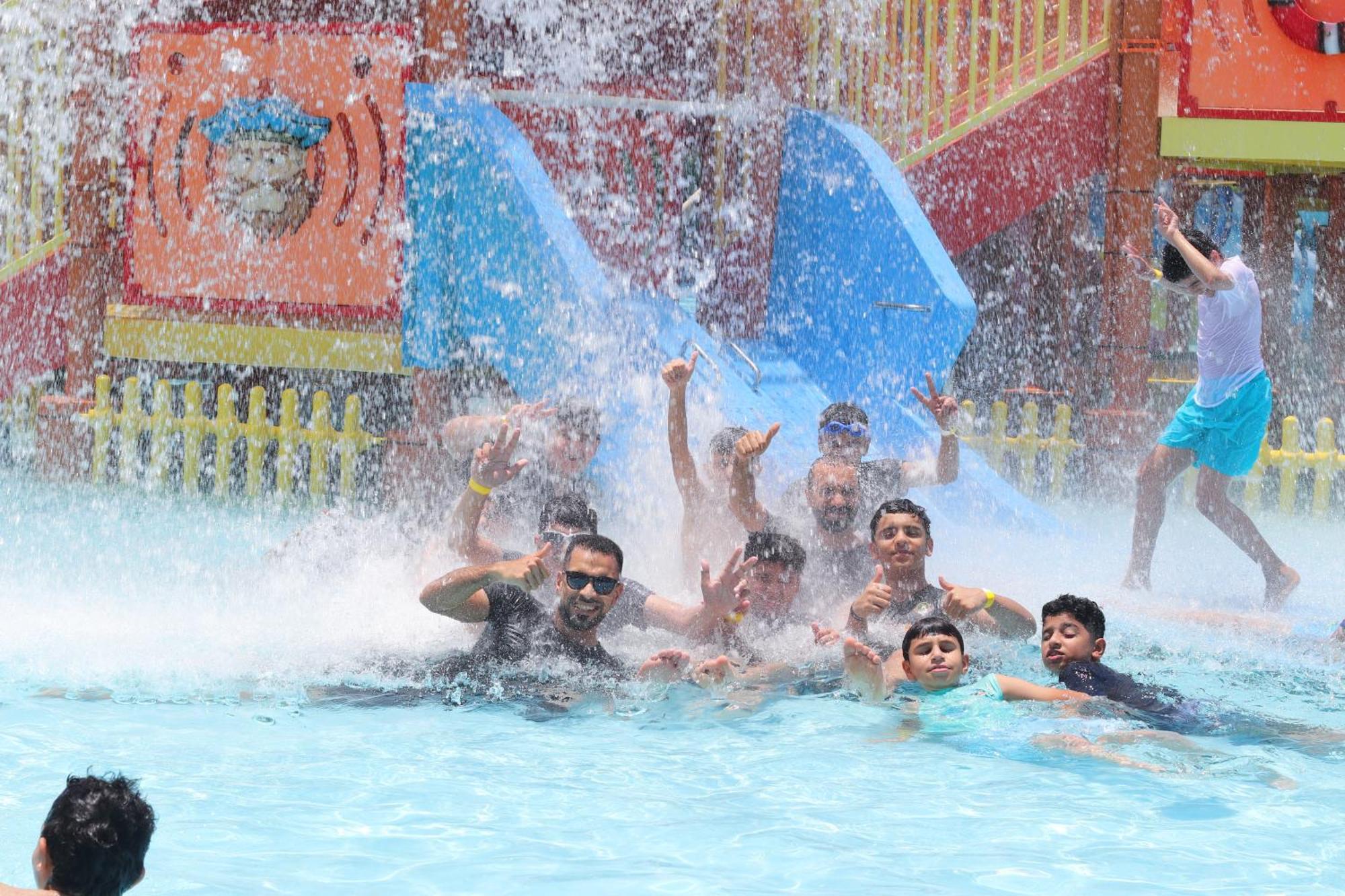 Lagoona Beach Luxury Resort And Spa Manama Exterior foto The photo shows a lively scene at a water park or pool area. Several people, including adults and children, are enjoying themselves in the water, splashing and posing for the camera. Water is cascading down, creating a refreshing atmosphere. In the b