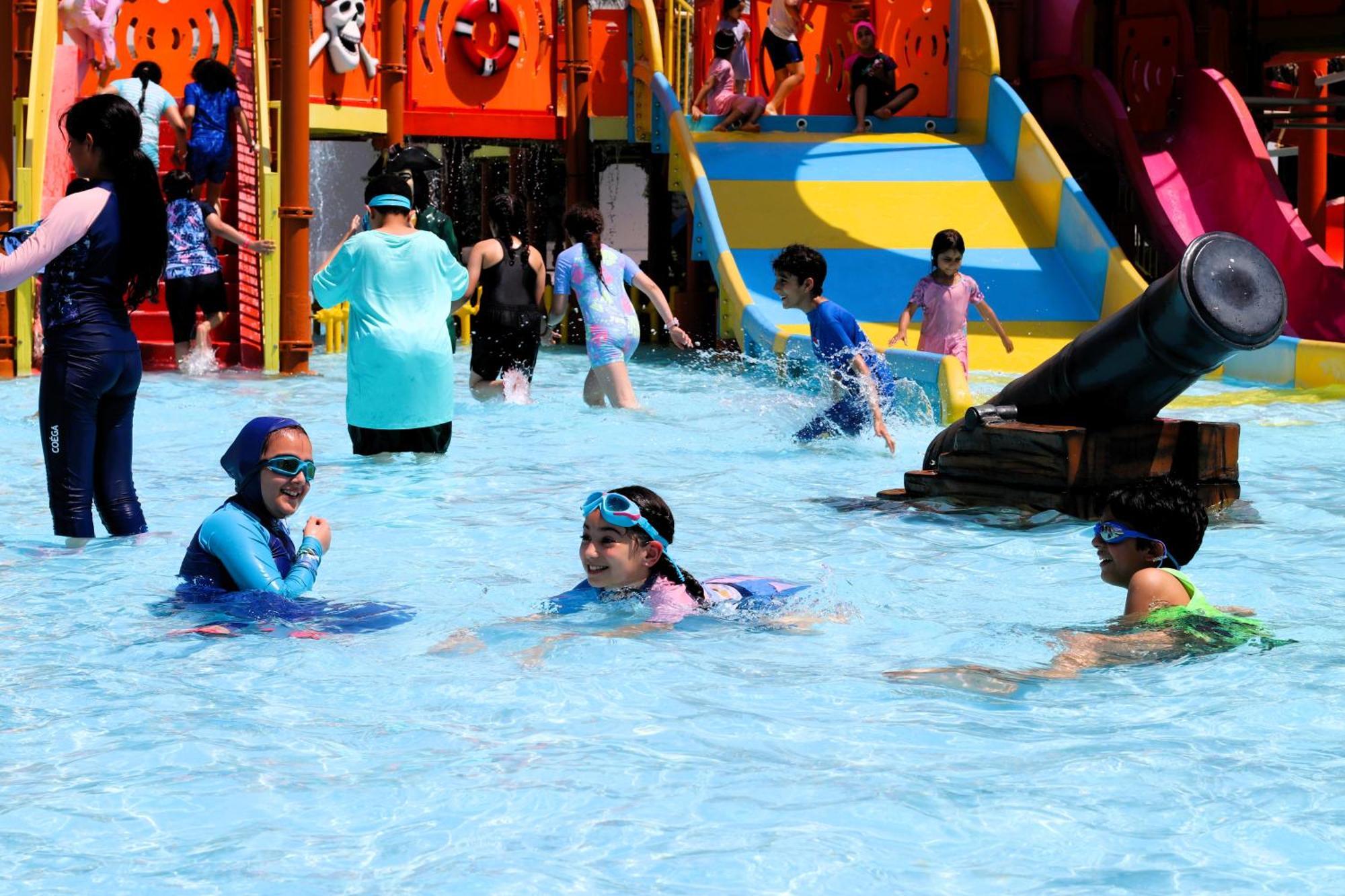 Lagoona Beach Luxury Resort And Spa Manama Exterior foto The photo shows a vibrant water park scene with several children playing in a shallow pool. Some are swimming and splashing around, while others are playing on colorful slides in the background. The atmosphere is lively and cheerful, with kids of var