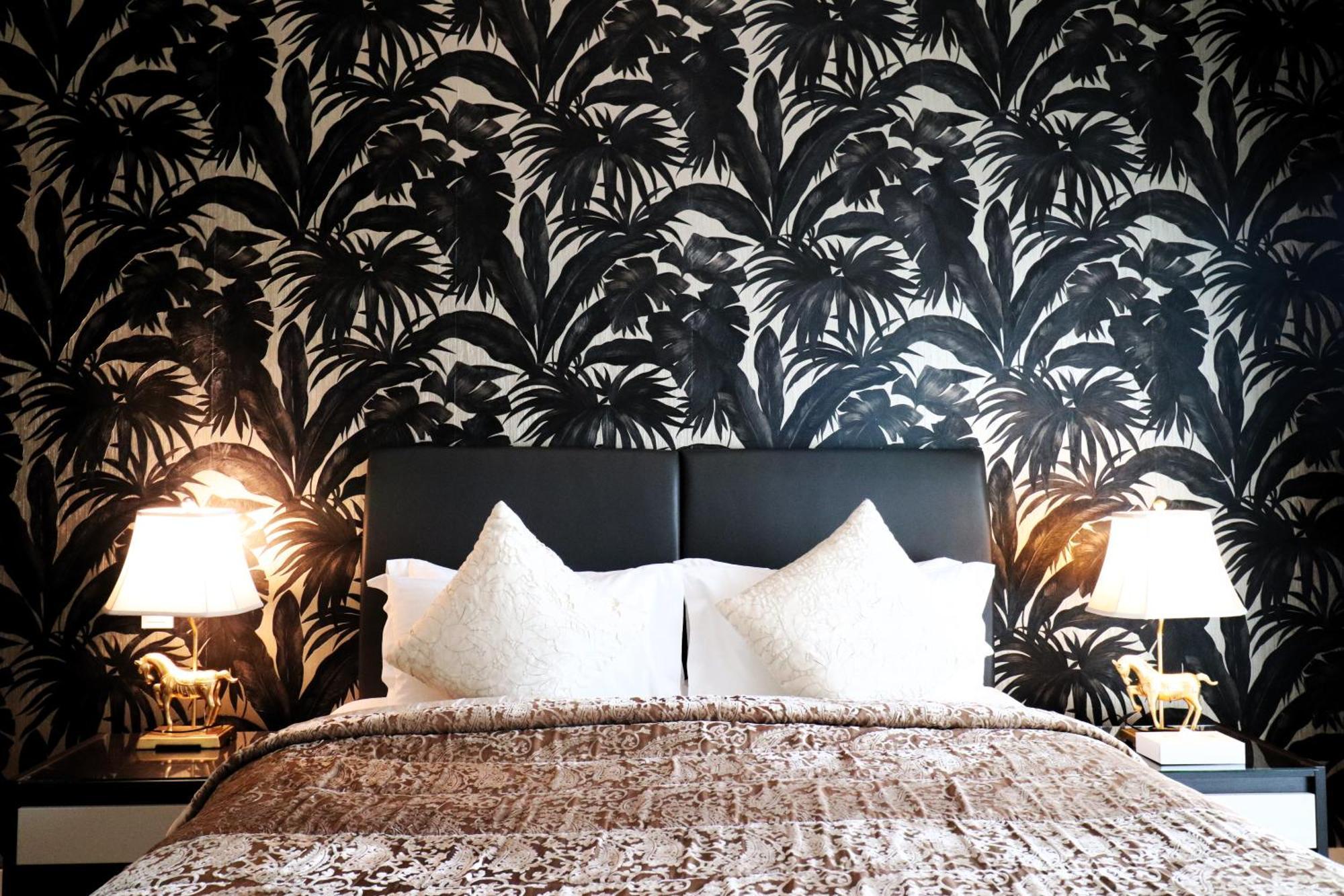 Lagoona Beach Luxury Resort And Spa Manama Exterior foto The photo depicts a stylish bedroom featuring a distinctive wall covered in a black and white tropical foliage wallpaper. The bed has a modern black headboard and is adorned with white pillows, creating a clean and elegant look. A textured brown thro